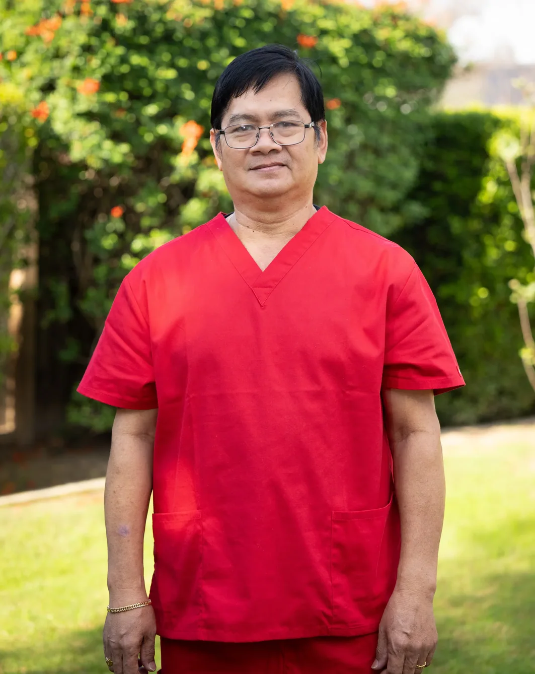 Caregiver in red medical scrubs standing in outdoor garden area