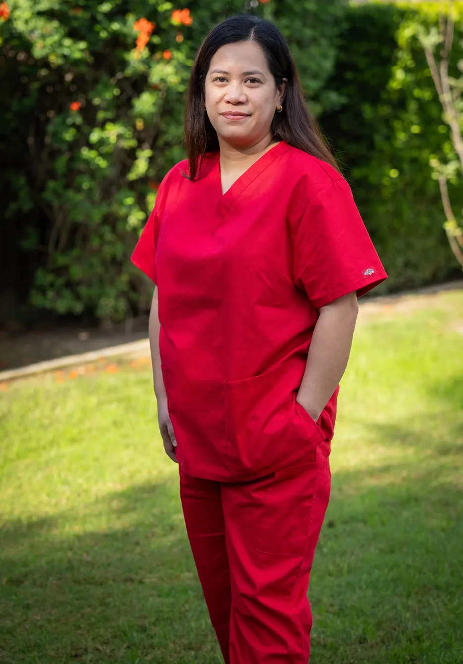 Care professional in red medical scrubs posing in outdoor garden setting