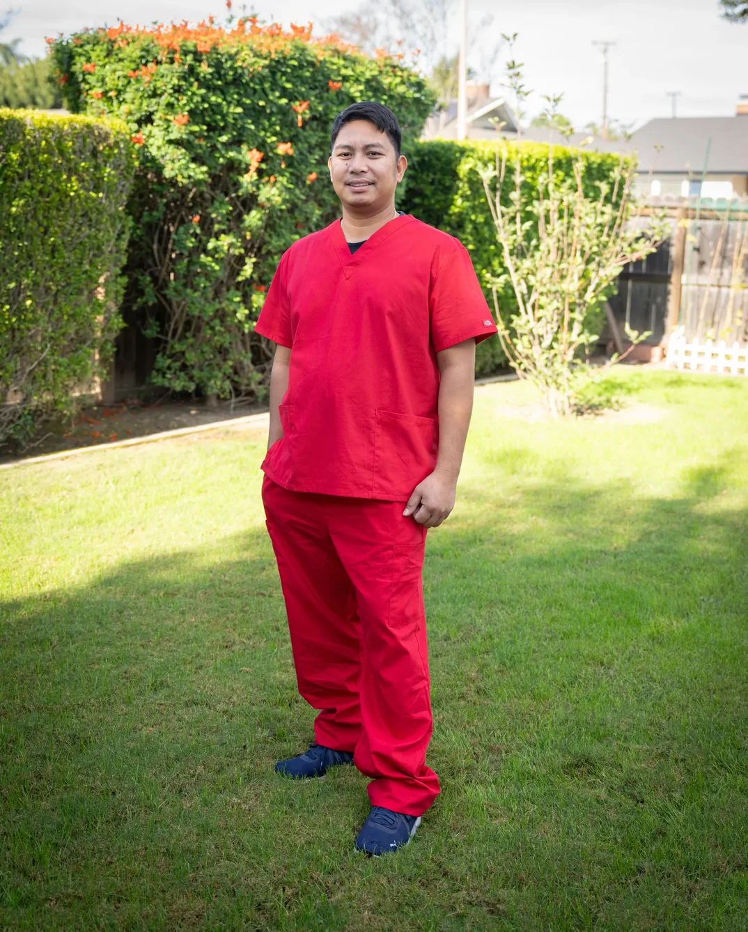 Professional caregiver in red medical scrubs standing in facility garden